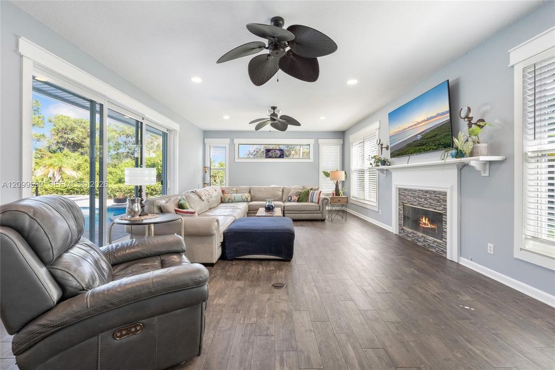Living area featuring wood-finish flooring, a stone-surround fireplace, dual ceiling fans, and expansive sliding glass doors