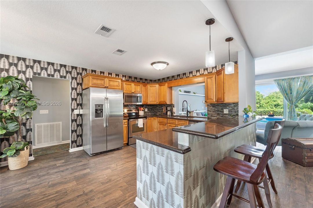 Kitchen featuring wood cabinetry, stainless steel appliances, stacked stone backsplash, and a breakfast bar with stone-finish countertop and pendant lighting