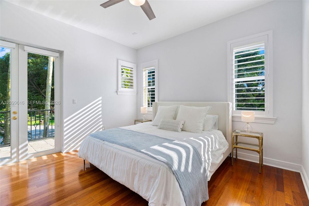 Wood-finish flooring, plantation shutters, full-height glass door, and a ceiling fan with integrated lighting