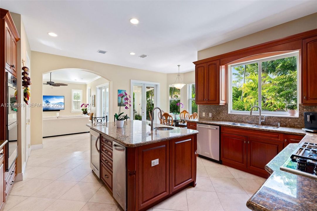 Kitchen featuring rich wood cabinetry, stone-surface countertops, central island with integrated prep sink, stainless steel appliances, and large picture window