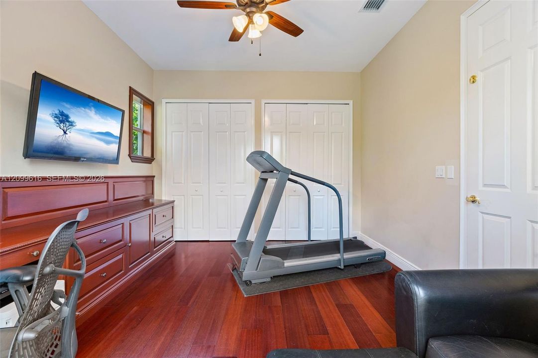 Wood-finish flooring, custom built-in cabinetry with integrated desk surface, dual bi-fold closets, and ceiling fan with integrated lighting
