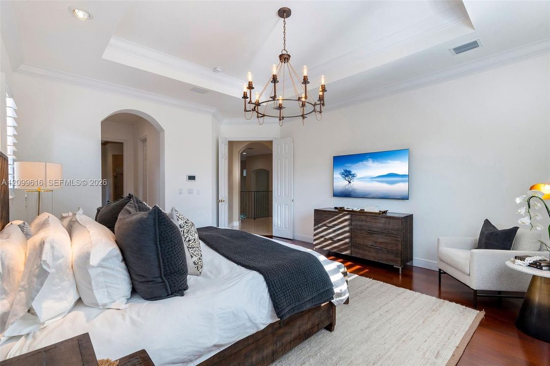 Tray ceiling featuring crown molding and a multi-arm iron chandelier, wood-finish flooring, and arched entryway