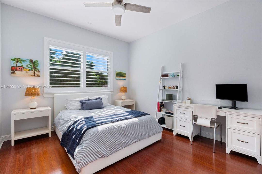 Room featuring wood-finish flooring, white plantation shutters, and a ceiling fan