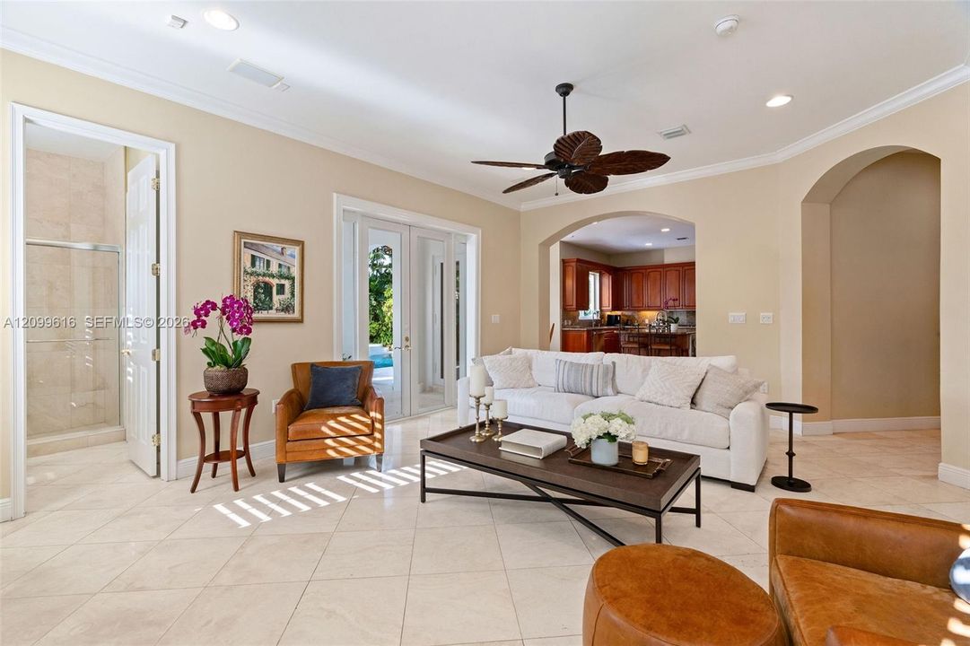 Interior space featuring large-format tile flooring, arched wall openings, crown molding, a ceiling fan with leaf-style blades, and glass-paned double doors
