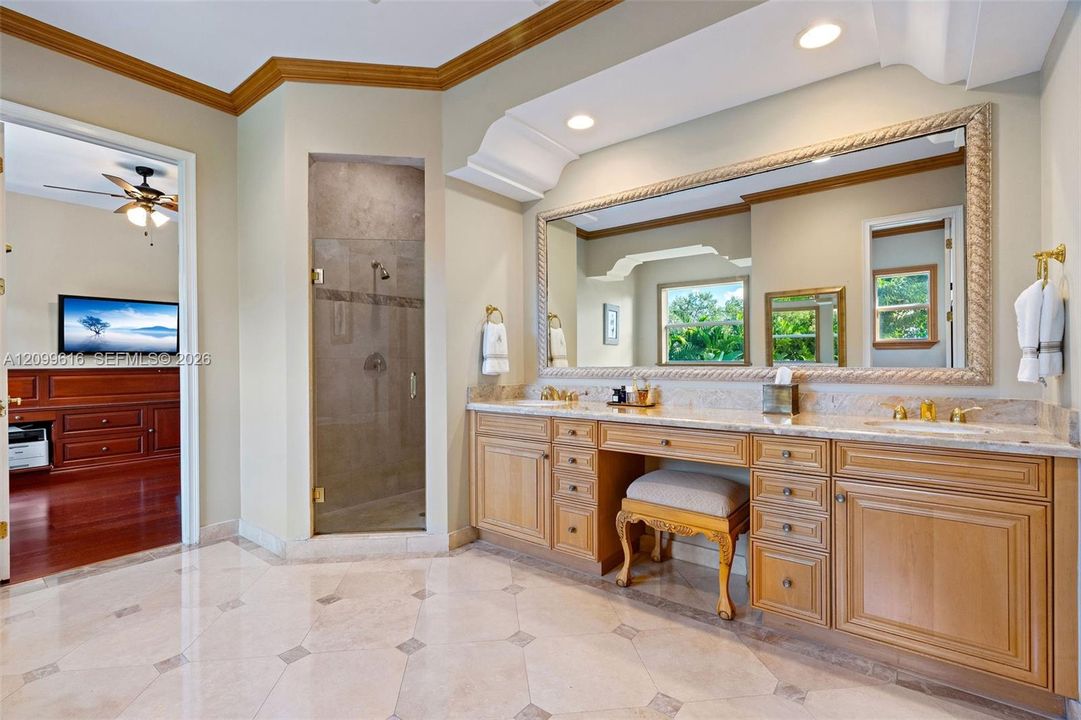 Custom dual-sink vanity with light wood-finish cabinetry, natural stone countertops, recessed lighting, and a large framed mirror