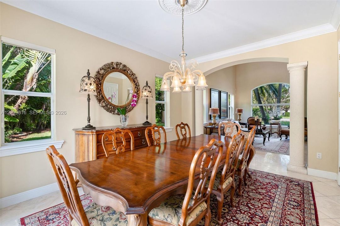 Dining area featuring tile flooring, a decorative ceiling medallion with a chandelier, crown molding, and an arched entryway supported by a column