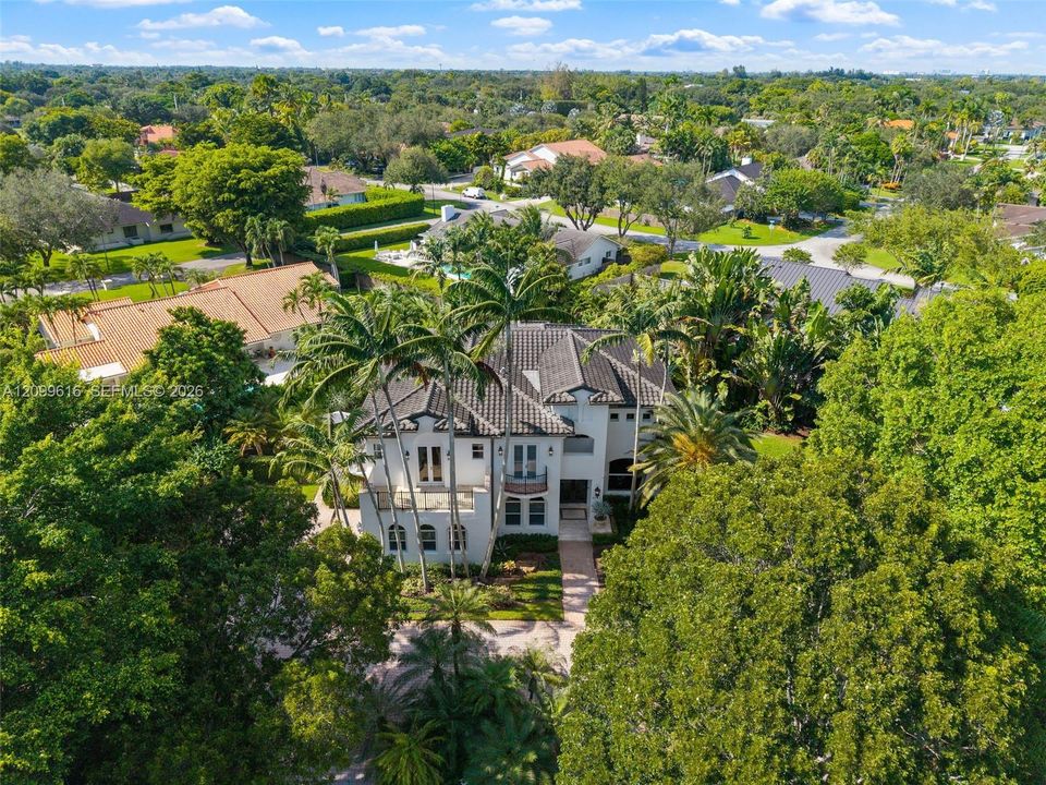 Multi-story estate featuring a concrete tile roof, stucco exterior, multiple covered balconies, arched architectural detailing, and extensive mature landscaping