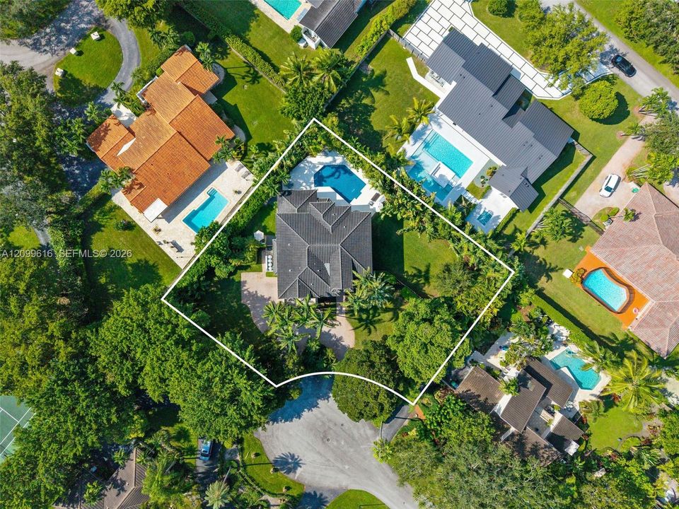 Aerial perspective featuring a multi-hipped roofline, an in-ground swimming pool, stone-paver hardscaping, mature landscaping, and a corner lot configuration