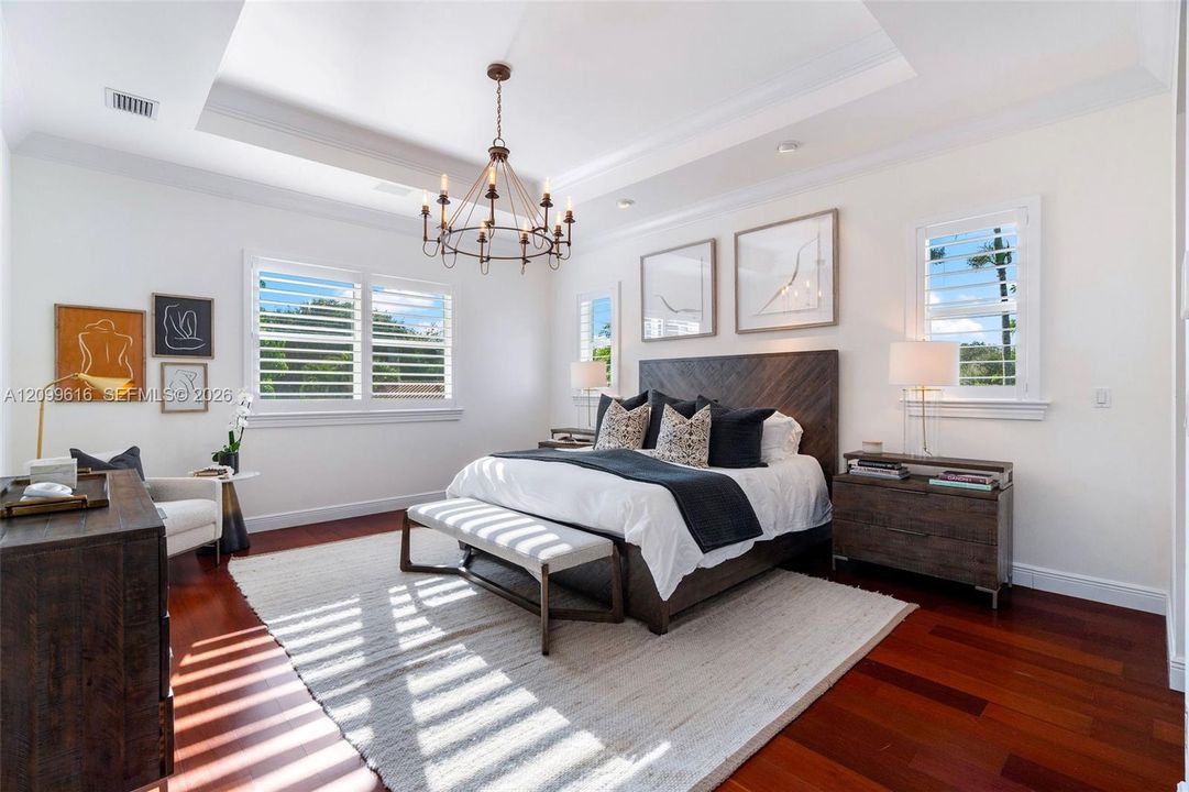 Tray ceiling, wood-finish flooring, plantation shutters, and multi-tiered iron chandelier