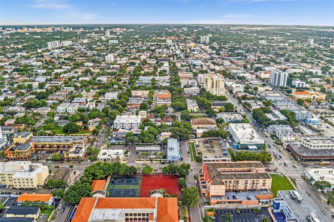 Aerial perspective showcasing a dense urban landscape with varied architectural styles, extensive tree canopy, and multiple commercial and residential buildings