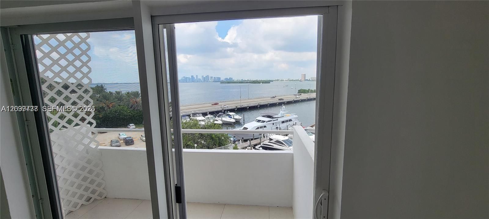 Private balcony featuring tiled flooring, solid wall railings, and a lattice privacy screen, showcasing water, marina, and city skyline scenery
