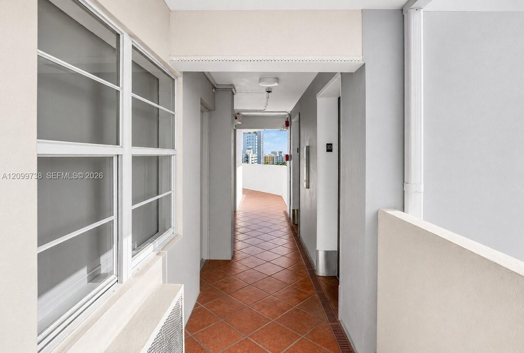 Exterior corridor featuring diamond-patterned terracotta tile flooring, white-framed windows, and a neutral color palette