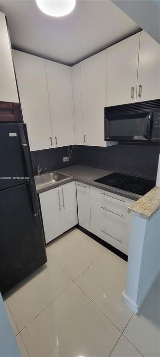 Kitchen featuring white cabinetry, dark stone-finish countertops, tile flooring, and integrated black appliances