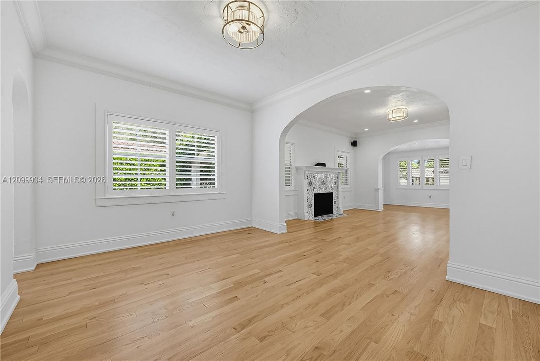 Interior featuring wood-finish flooring, decorative arched entryways, a fireplace with patterned tile surround, plantation shutters, and recessed lighting