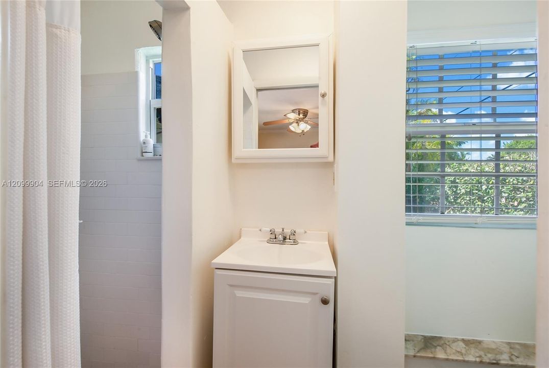 White vanity with an integrated basin, chrome-finished dual-handle faucet, white framed medicine cabinet, and a shower area featuring white wall tile