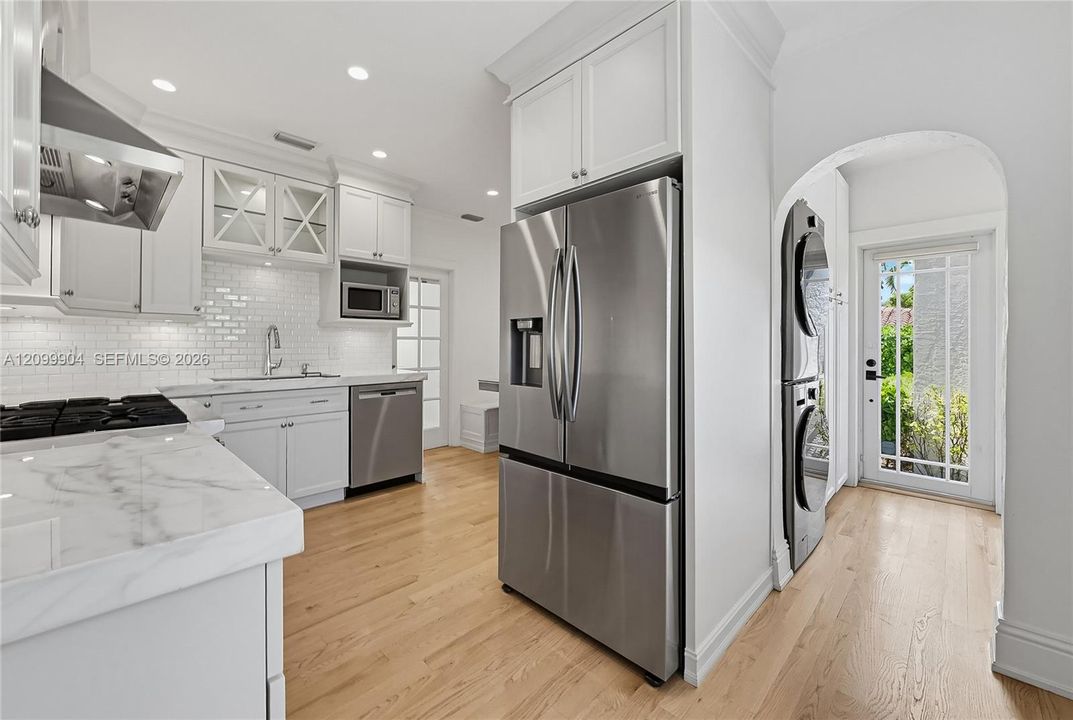 Kitchen featuring white shaker-style cabinetry, stone countertops, subway tile backsplash, stainless steel appliances, and wood-finish flooring