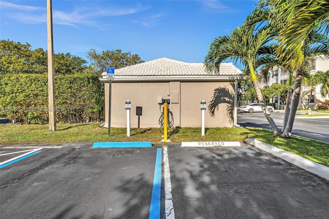 Electric vehicle charging station featuring a wall-mounted unit, asphalt parking area, and painted stall demarcations