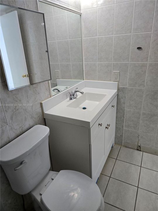 Bathroom featuring a white vanity cabinet with an integrated sink and chrome faucet, rectangular wall mirror, and ceramic tile flooring and wall surfaces
