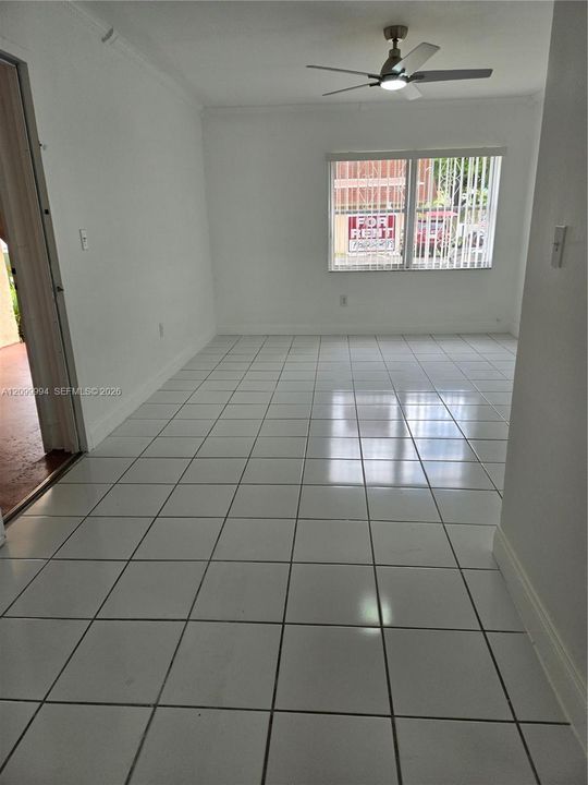 Neutral-toned interior space featuring white ceramic tile flooring, a mounted ceiling fan with integrated lighting, and a window with vertical blinds