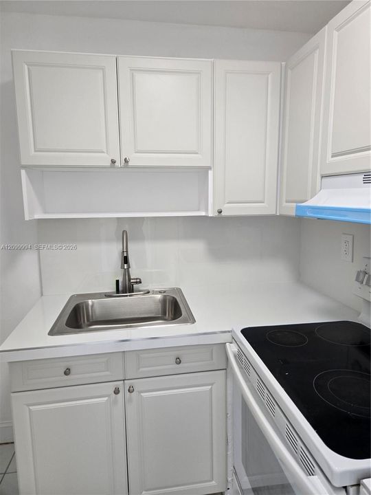 Kitchen featuring white cabinetry, solid surface countertop, stainless steel drop-in sink with a high-arch faucet, and an integrated electric cooktop