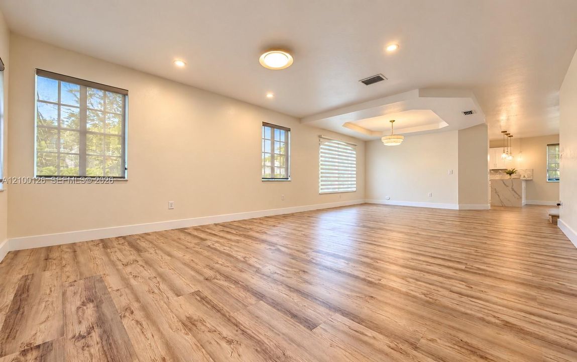 Open-concept interior featuring wood-finish flooring, tray ceiling with recessed lighting, multi-pane windows, and a suspended chandelier