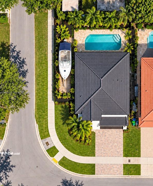 Aerial perspective featuring a dark-tiled hipped roof, a paved paver driveway, an in-ground swimming pool, and side-yard boat storage