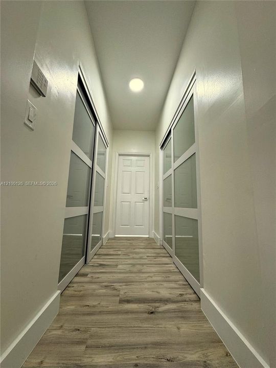 Hallway featuring wood-finish flooring, two sets of sliding closet doors with frosted glass panels, and a paneled interior door with metal hardware