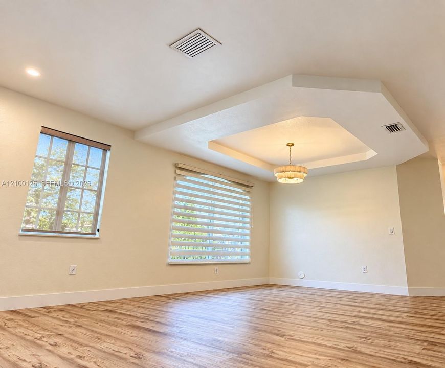 Tray ceiling with a tiered architectural design, wood-finish flooring, recessed lighting, and multi-pane windows