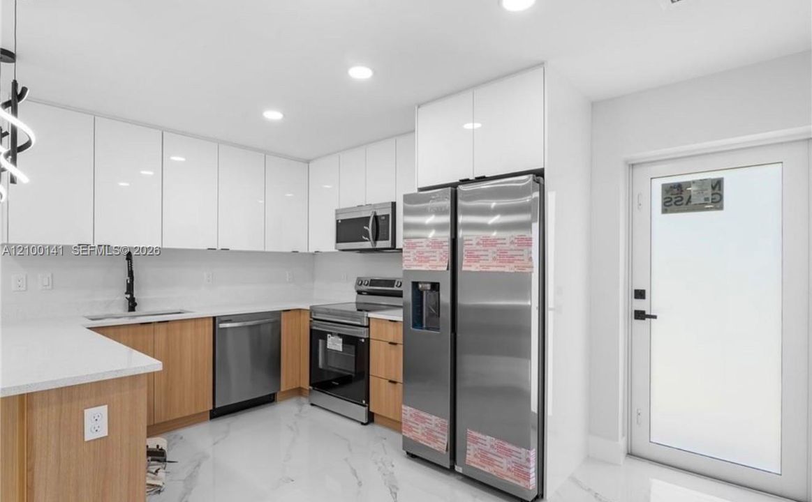Kitchen featuring white upper cabinetry, wood-finish lower cabinetry, stone-style countertops, stainless steel appliances, and large-format tile flooring