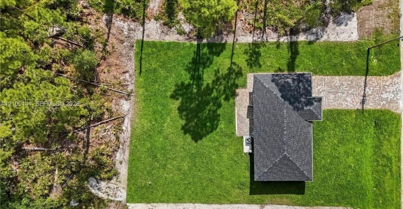 Aerial perspective featuring a rectangular lot, mature perimeter trees, expansive lawn area, paved driveway, and shingled roof