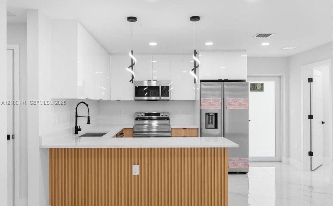 Kitchen featuring flat-panel white cabinetry, white stone-finish countertops, stainless steel appliances, a wood-slat breakfast bar, and decorative spiral pendant lighting