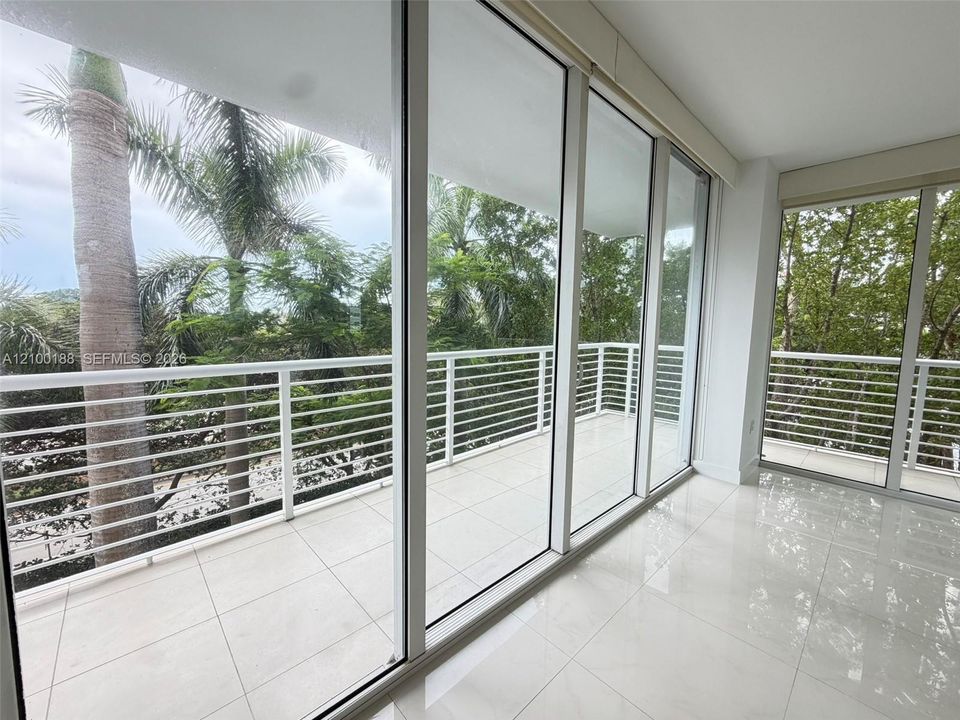 Floor-to-ceiling glass sliding doors, white tiled flooring, and a wrap-around balcony featuring white horizontal railings