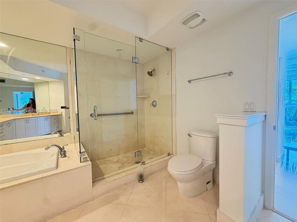 Bathroom featuring a tiled shower stall with a glass enclosure, built-in soaking tub with stone surround, wall-to-wall vanity mirror, and neutral tile flooring