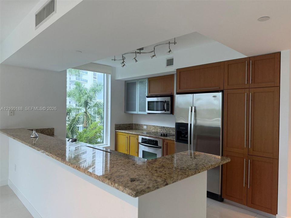 Kitchen featuring stone countertops, breakfast bar, built-in cabinetry with glass-panel upper doors, stainless steel appliances, and track lighting