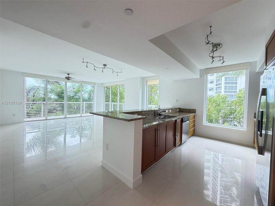 Open concept kitchen featuring stone countertops, wood-finish cabinetry, stainless steel appliances, large-format tile flooring, and floor-to-ceiling windows