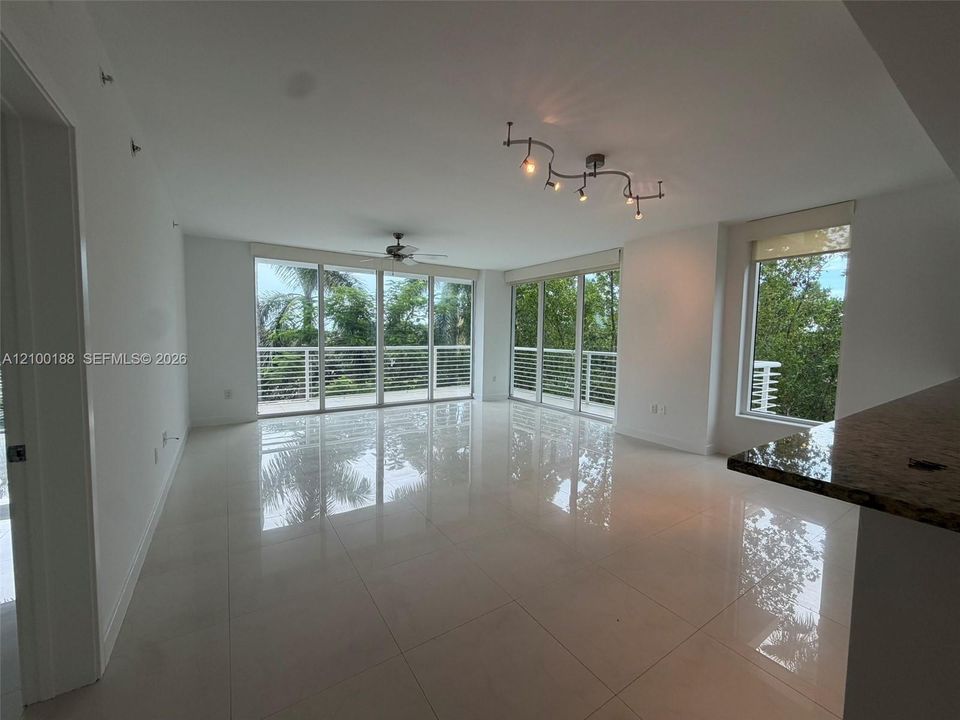 Open-concept interior featuring large-format tile flooring, expansive floor-to-ceiling windows, track lighting, a ceiling fan, and a stone-surface breakfast bar