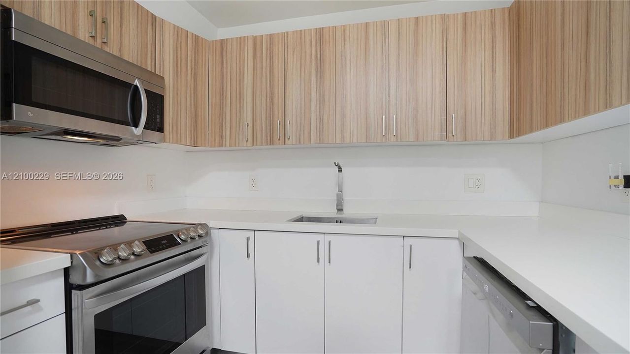 Kitchen featuring light wood-finish cabinetry, solid white countertops, stainless steel appliances, and a single-basin sink