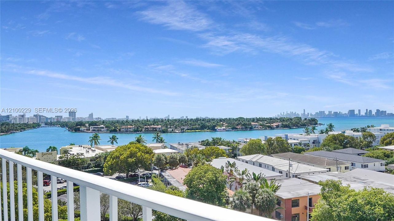 Elevated terrace with a white metal railing overlooking a waterfront expanse, coastal landscape, and a distant city skyline