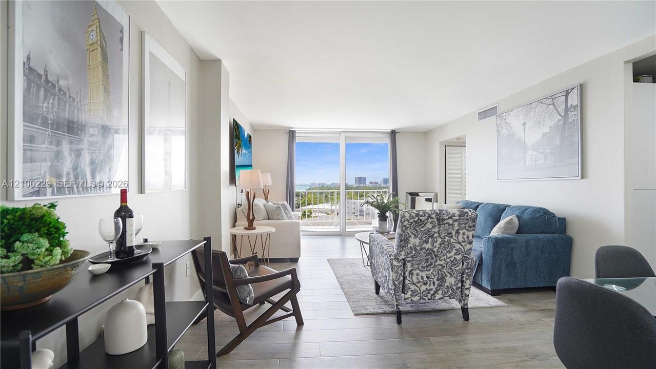 Open-concept interior featuring light wood-finish tile flooring, neutral wall tones, and floor-to-ceiling glass sliding doors leading to a balcony