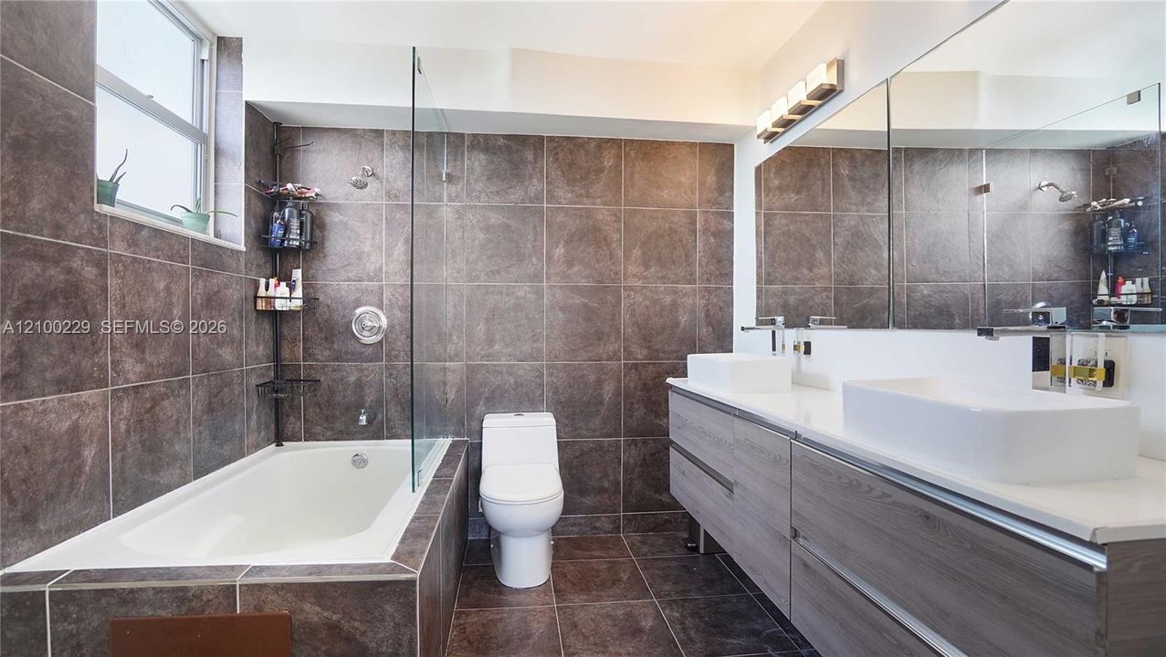 Bathroom featuring a floating double vanity with rectangular vessel sinks, a glass-enclosed shower and tub combination, full-width wall mirror, and floor-to-ceiling tile surround