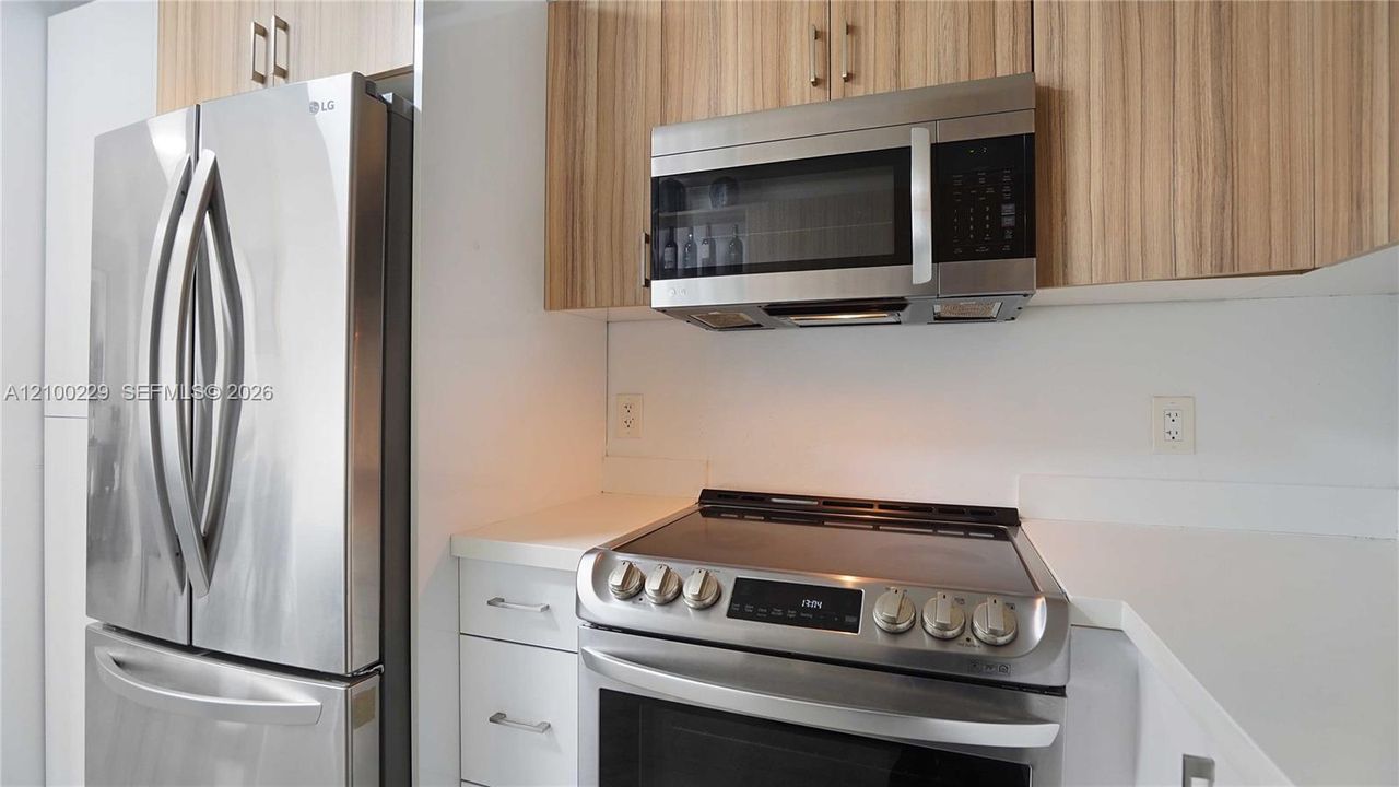 Stainless steel french-door refrigerator, matching over-the-range microwave, electric range with glass cooktop, solid-surface countertops, and wood-finish cabinetry