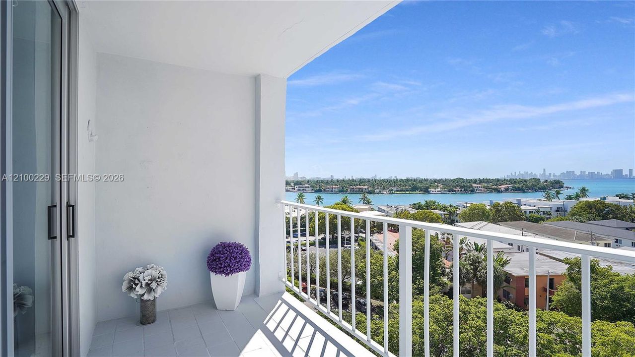 Covered balcony featuring tile flooring and a white metal railing, overlooking the water and metropolitan skyline