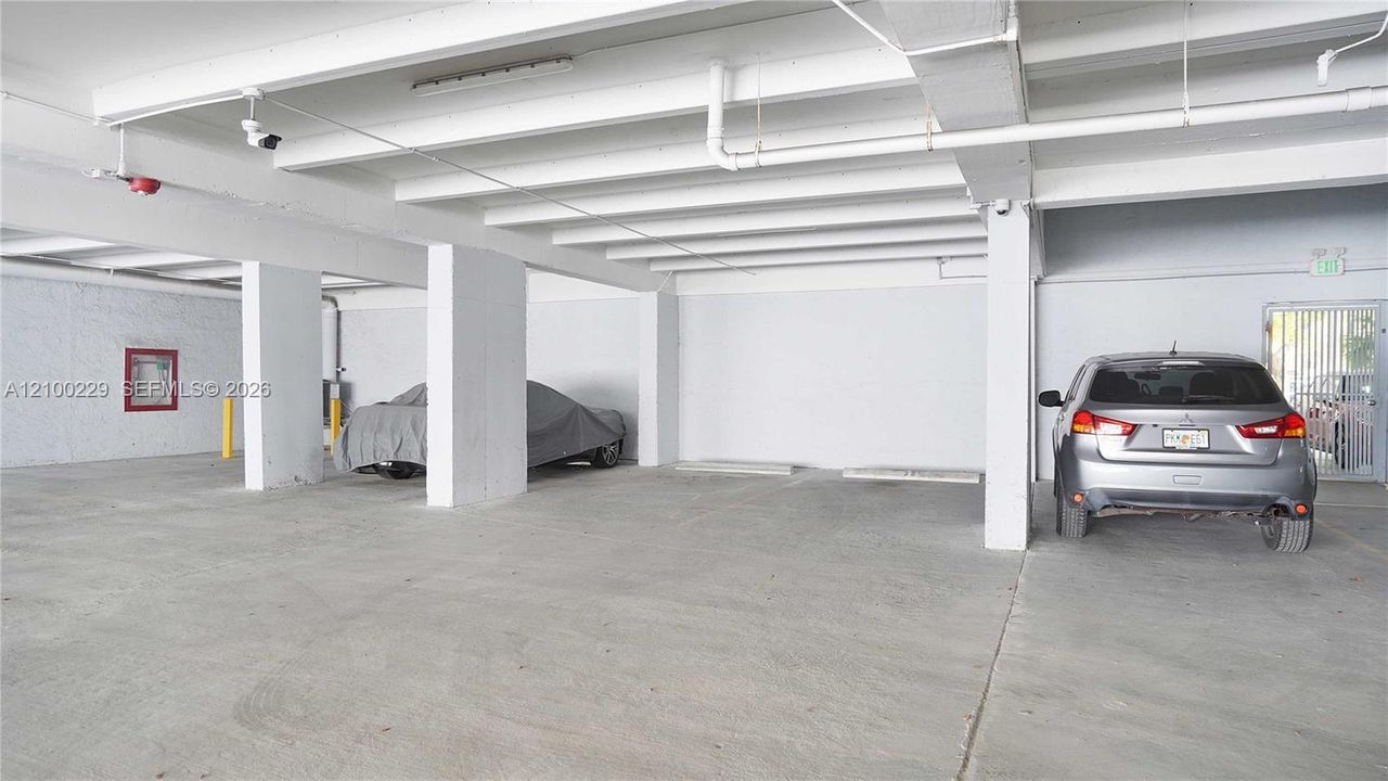 Covered parking area featuring structural concrete columns, a painted concrete floor, exposed ceiling joists, and security lighting