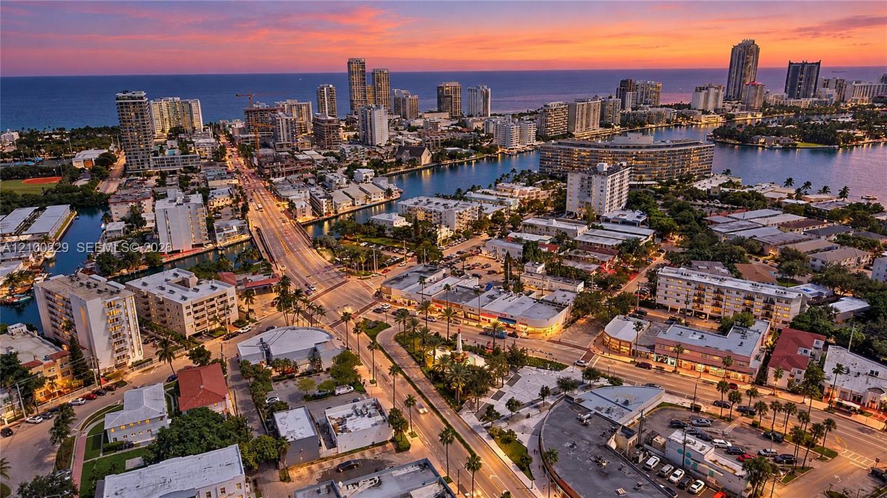 Aerial perspective of an urban coastal district featuring waterways, high-rise residential buildings, and prominent ocean horizon