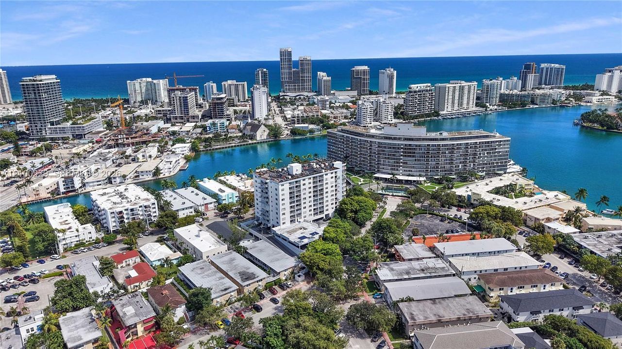 Aerial perspective of coastal residential district featuring waterfront positioning, proximity to ocean shoreline, dense canopy foliage, and high-rise development