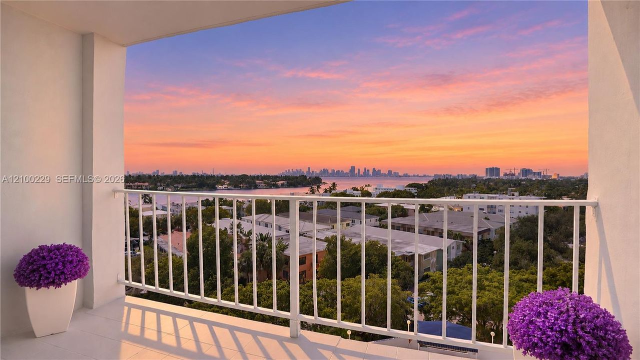 Covered balcony featuring white tile flooring and a white metal railing overlooking a cityscape and water