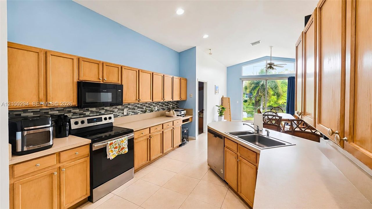 Kitchen finish countertops, mosaic tile backsplash, stainless steel appliances, and vaulted ceilings with recessed lighting
