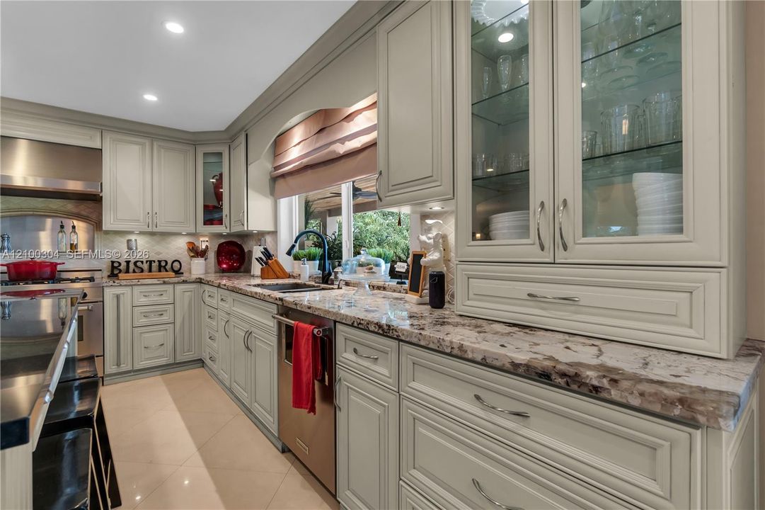 Kitchen featuring light-toned cabinetry with glass-front display uppers, stone-patterned countertops, stainless steel appliances, and tile flooring