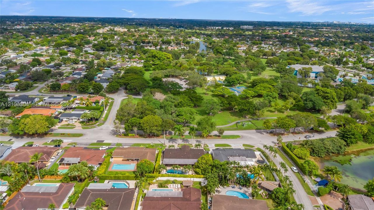 Aerial perspective of a suburban landscape featuring a dense canopy of mature trees, expansive green space, paved street networks, and residential properties with integrated swimming pools