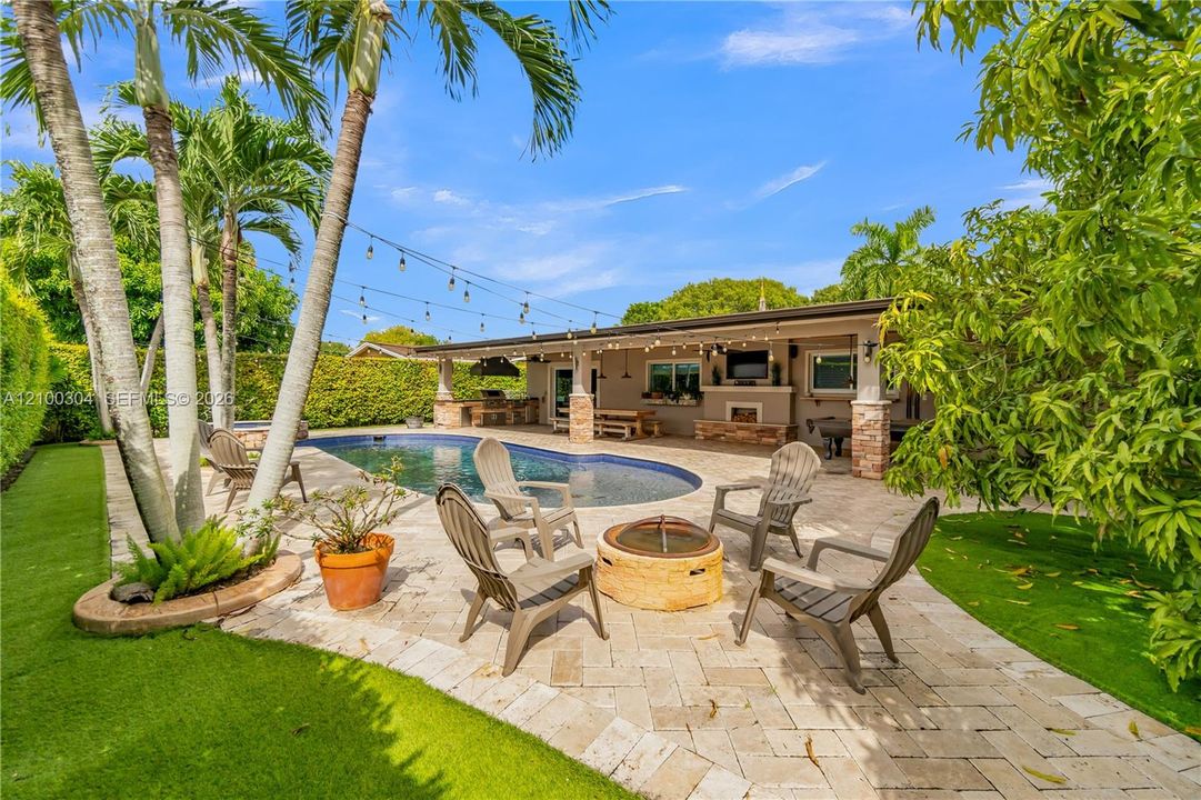 Backyard oasis featuring an in-ground pool, stone-paver patio, covered outdoor kitchen, and manicured landscaping